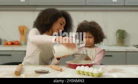 Mamma afro-americana aiuta la bambina a cucinare insieme a preparare l'impasto in cucina la famiglia felice prepara gli ingredienti della torta torta torta pasticceria bambino Foto Stock