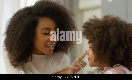 Famiglia felice in cucina casalinga cucinare insieme madre afroamericana con bambino bambino bambina insegnare a cuoca figlia giocare toccare naso con le dita sporco Foto Stock