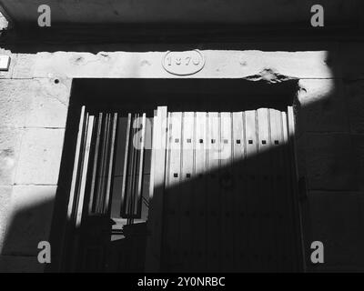 Porta d'ingresso in legno d'epoca sul muro di pietra illuminata dalla luce del sole in bianco e nero Foto Stock