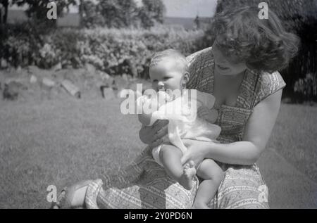 anni '1950, storica, in un giorno d'estate, fuori in un giardino, una nuova madre con la sua bambina Foto Stock