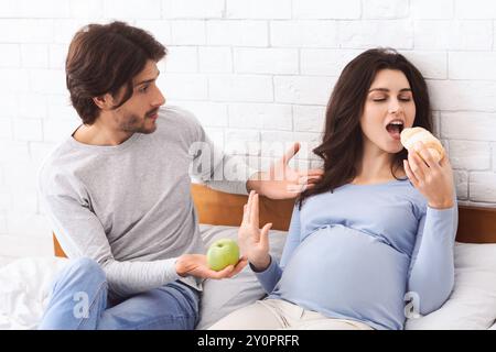 Donna incinta affamata che mangia croissant al posto della mela verde Foto Stock