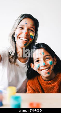 Famiglia, bambina felice e madre che si divertono con il viso dipinto a casa. Mamma latina POV che fa selfie Foto Stock