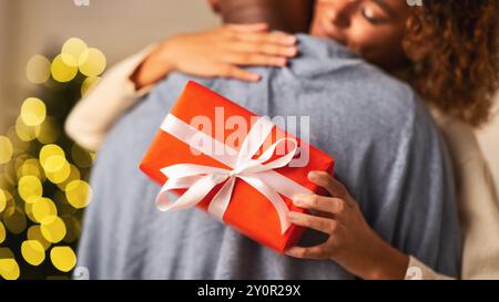Amorevole donna afro abbracciando il marito, tenendo regalo di natale Foto Stock