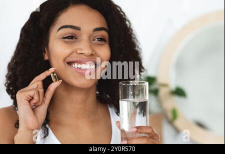 Assunzione giornaliera di vitamine. Happy Black Woman capsula di tenuta pillola e vetro dell'acqua Foto Stock