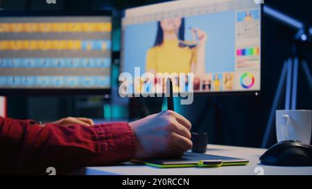 Editor di foto editing di immagini, correzione del colore in un'azienda di post-produzione tramite tavoletta grafica. Fotografo che fissa le foto sovraesposte con lo stilo sul dispositivo touchscreen, primo piano Foto Stock