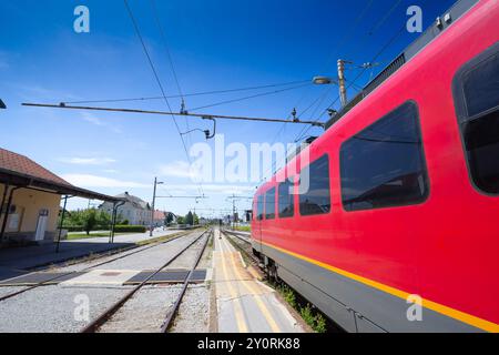Treno elettrico sloveno che entra nella stazione di Skofja Loka in una giornata limpida. Il moderno treno rosso riflette la robusta infrastruttura di trasporto pubblico di Foto Stock