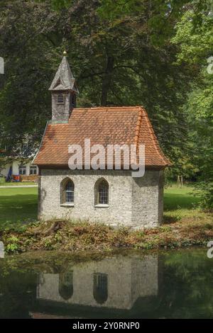 Una piccola casa in pietra con un tetto piastrellato rosso sorge sul bordo di uno stagno, circondato da una fitta foresta, Alpi, Austria, Europa Foto Stock