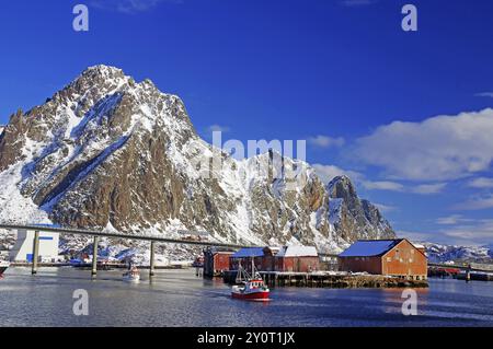 Porto con ponte, circondato da montagne innevate, barche in acqua e capannoni sulla riva, Lofoten, Svolvaer, Nordland, Artico, Norvegia, Europa Foto Stock