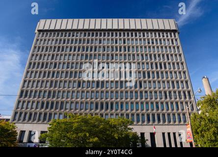 Un moderno edificio per uffici a più piani con finestre uniformi simili a una griglia domina la cornice. La struttura in cemento si erge contro un cielo blu brillante. Foto Stock