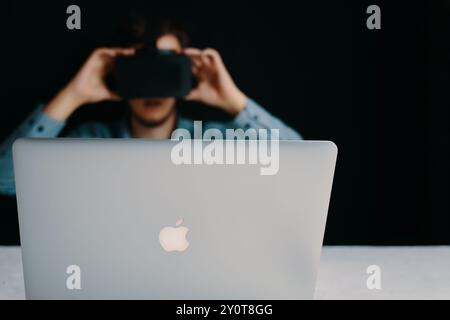 Uomo visivamente immerso nella realtà virtuale utilizzando un auricolare e un computer portatile alla scrivania in un ufficio Foto Stock