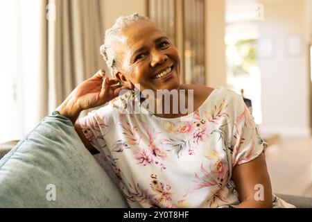 Donna anziana sorridente che si rilassa sul divano a casa, godendo momenti di pace Foto Stock