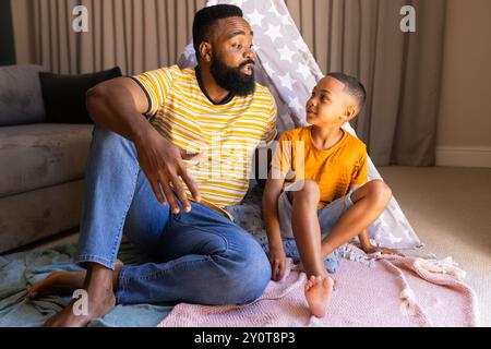 Padre e figlio seduti sul pavimento, che parlano e si legano in un ambiente accogliente Foto Stock