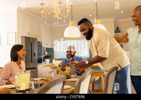 Serve cibo al tavolo da pranzo, famiglie multi-generazionali che mangiano insieme Foto Stock