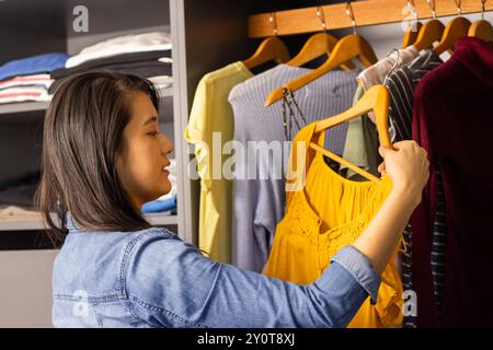 Donna asiatica che sceglie l'abito giallo dal guardaroba, organizza i vestiti nell'armadio Foto Stock