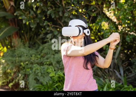 Utilizzando il visore VR, donna che gioca a un gioco di realtà virtuale all'aperto in giardino Foto Stock