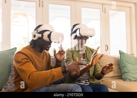 Utilizzando i visori VR, una coppia afroamericana si gode un'esperienza di realtà virtuale sul divano Foto Stock