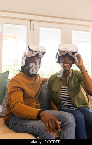 Utilizzando i visori VR, una coppia afroamericana felice che si gode un'esperienza di realtà virtuale a casa Foto Stock