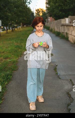 Ekaterinburg, Russia, 14 febbraio 2024: Cute girl Outdoors solving a cubo puzzle il cubo di rubik. Fu inventato dall'architetto ungherese Erno Rubik nel 19 Foto Stock