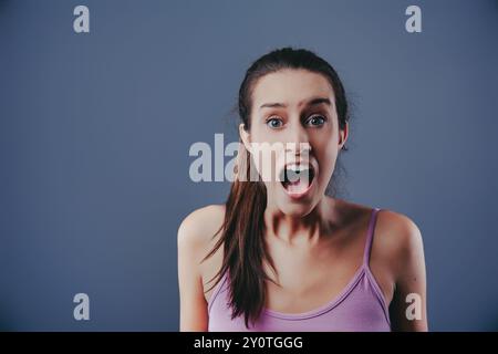 La giovane donna sta vivendo un momento di forte shock o sorpresa, con la bocca spalancata in un urlo mentre reagisce a qualcosa di inaspettato Foto Stock