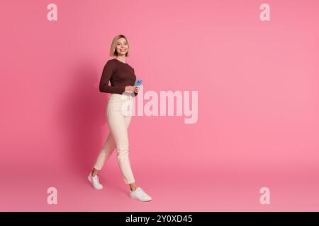 Foto di una giovane ragazza bionda allegra con dolcevita arancione e jeans in sella al carrello del supermercato mostrano un segno V isolato su sfondo di colore viola Foto Stock