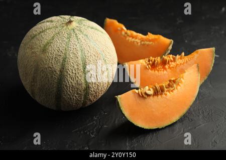 Meloni Cantaloupe maturi tagliati e interi su un tavolo con texture scura Foto Stock