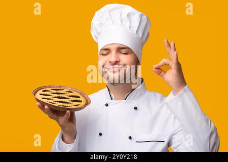 Piacere Baker Holding Pie Gesturing Okay Su Sfondo Giallo, Panorama Foto Stock