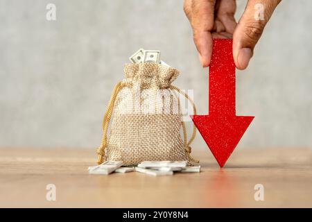 Un sacco pieno di banconote da un dollaro e una mano tiene una grande freccia rossa rivolta verso il basso. Perdita finanziaria, recessione del mercato o recessione economica co Foto Stock