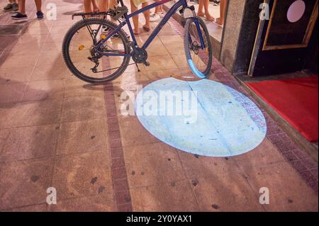 Immagine di una bicicletta su una strada acciottolata di notte, con una luce blu proiettata sul terreno, che crea un'atmosfera urbana e misteriosa. Foto Stock