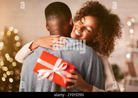 Grati afro donna con un regalo di Natale abbracciando il marito a casa Foto Stock