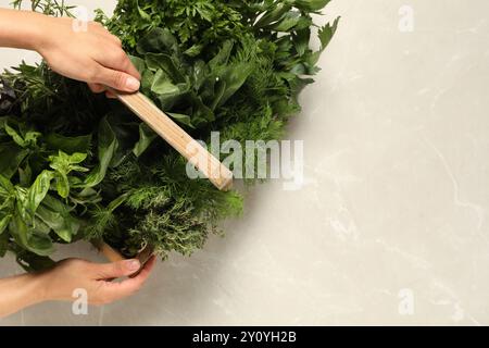 Donna che tiene diverse erbe fresche in un cestello di legno al tavolo leggero, vista dall'alto. Spazio per il testo Foto Stock