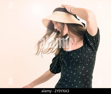 Giovane donna che regge il cappello ondeggiando con un ritratto del movimento dei capelli Foto Stock