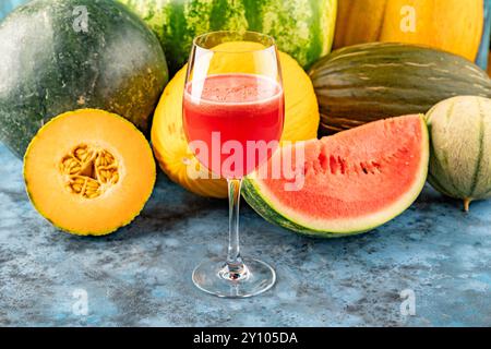L'anguria e il melone bevande fresche spremute in bicchiere. La bevanda è su sfondo blu con metà anguria e melone sullo sfondo Foto Stock