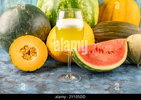 L'anguria e il melone bevande fresche spremute nel bicchiere. La bevanda è su sfondo blu con metà anguria e melone sullo sfondo Foto Stock