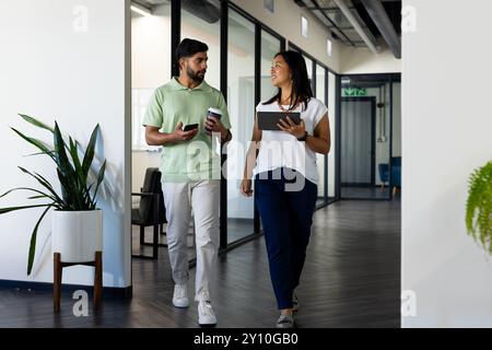 Camminare in ufficio, i colleghi discutono di lavoro mentre si tiene un caffè e un tablet Foto Stock