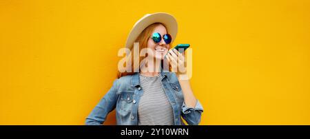 Giovane donna felice sorridente che tiene in mano la conversazione al telefono, ragazza gioiosa che usa lo smartphone, prende le chiamate indossando abiti casual su un colorato dorso giallo Foto Stock