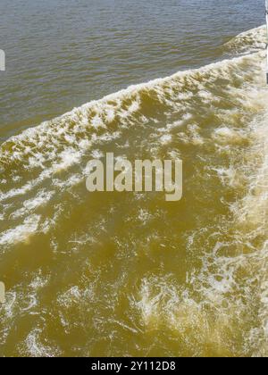 Primo piano di turbolenti schemi d'acqua e schiuma creata dall'elica della barca nel fiume verdastro Foto Stock