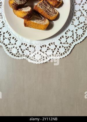 Pezzi singoli di torta di marmo serviti su un piatto bianco su un topper rotondo di carta decorativa su sfondo grigio Foto Stock