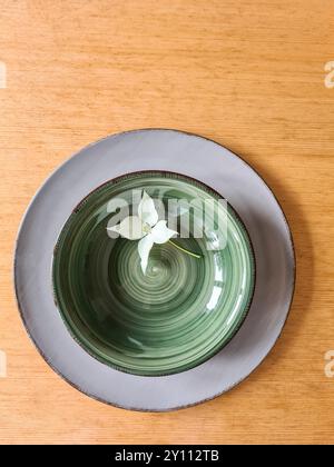 Un fiore bianco di legno di pino con stelo giace decorativamente su una ciotola verde con piatto Foto Stock