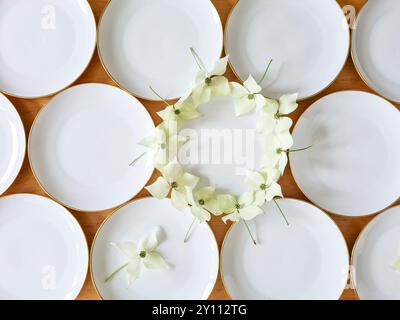 I piatti bianchi con un bordo d'oro sono decorati festosamente con i fiori della pianta del legno di cane, la preparazione e la decorazione per una celebrazione, la decorazione della tavola Foto Stock