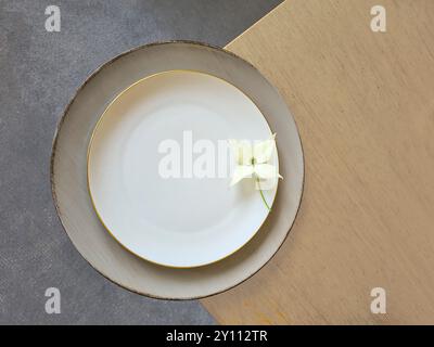 Un fiore bianco di legno di cane con stelo si trova decorativamente su un piatto bianco con un piattino grigio su un tavolo di legno Foto Stock