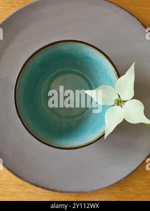 Un fiore bianco di legno di cane con 4 petali bianchi giace decorativamente su una ciotola verde turchese con piatto Foto Stock