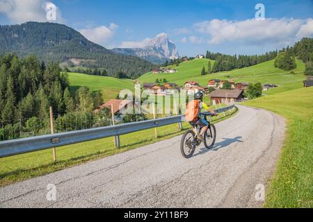 Italia, alto Adige, comune di San Martino in Badia / San Martino in Thurn. Ciclista sulla strada per il paese di Mir', sullo sfondo il Sass de Putia / Peitlerkofel, Dolomiti Foto Stock