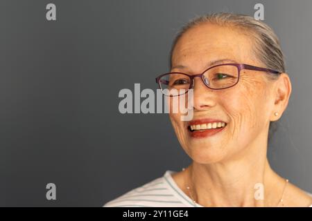 Sorridente anziana donna asiatica con occhiali che guardano lontano, mostrando felicità e soddisfazione Foto Stock