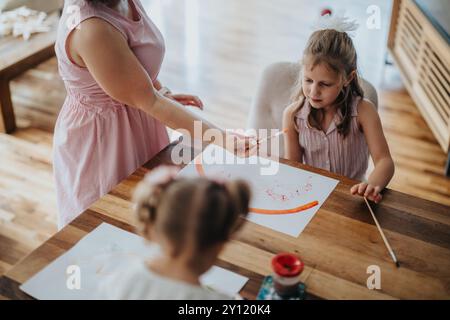 Giovane madre che disegna e dipinge con le sue due figlie piccole a casa Foto Stock