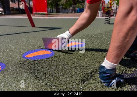 Nuovo parco giochi per bambini in costruzione. Una mano massaggiatrice con spatola e livellamento di morbide briciole di gomma pacciamatura in gomma per playgrou per bambini Foto Stock