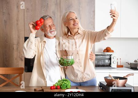 Coppia matura con i pomodori che fanno selfie in cucina Foto Stock