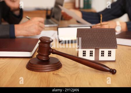 Modello di casa con il martelletto del giudice sul tavolo dell'avvocato durante la riunione in ufficio, primo piano Foto Stock