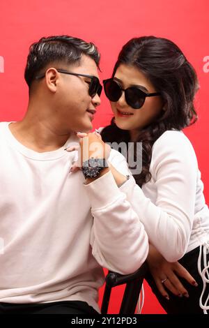 Una giovane coppia di uomini e donne asiatiche sorridenti che indossano maglioni bianchi, occhiali da sole, uomini che si guardano l'un l'altro tenendo per mano una foto informale. per roma Foto Stock
