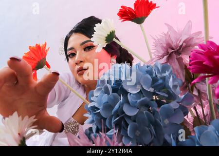 primo piano di una bella giovane ed elegante donna asiatica accanto a decorazioni floreali che indossano abiti tradizionali giavanesi moderni, abiti da sposa in velluto bianco Foto Stock