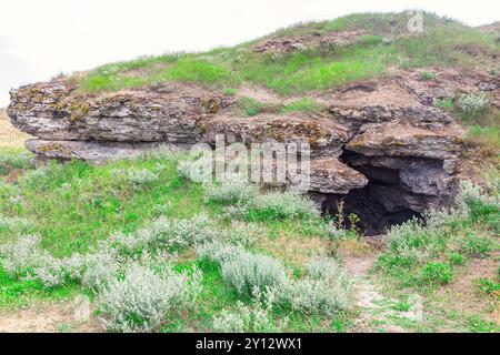 Collina rocciosa con una piccola grotta al centro. Campo erboso caratterizzato da una grotta con un piccolo ingresso, invitante esplorazione in mezzo al paesaggio naturale Foto Stock